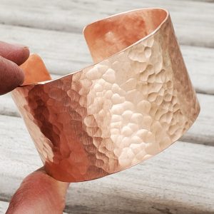 Wide hammered copper cuff bracelet held in maker's hand