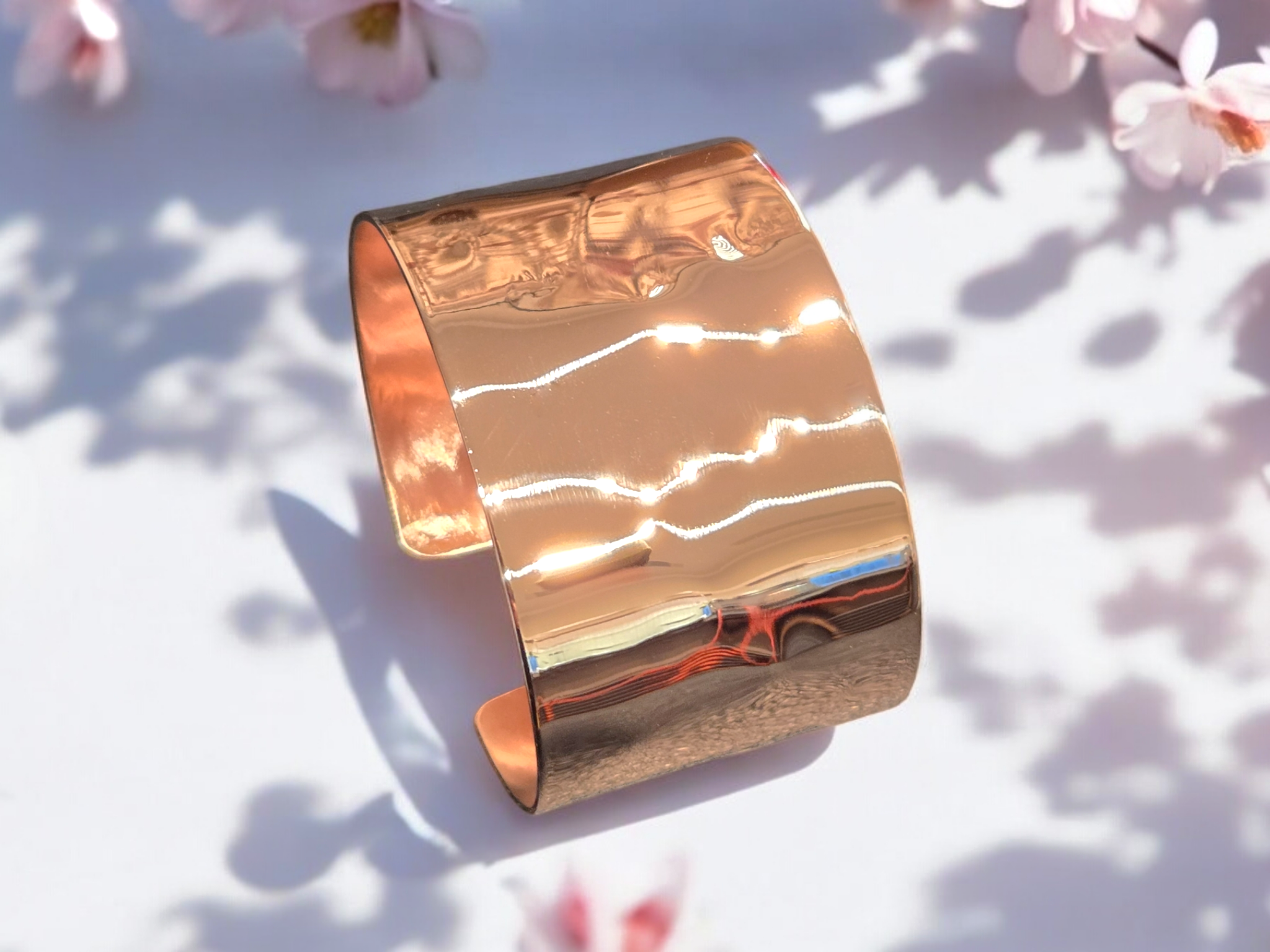 Wide Polished Hammered Copper Cuff Bracelet shown on a white background with spring flowers