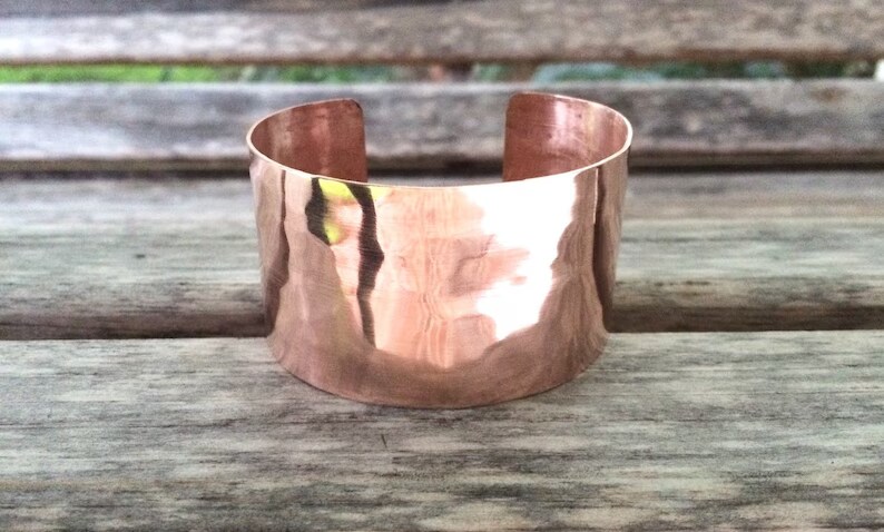 Cold Worked Hammered Copper Cuff Wide Bracelet shown highly polished on a wooden surface
