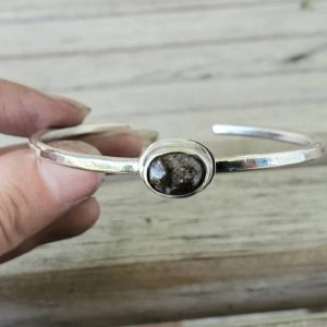 Black Agate Cabochon in Sterling Bezel Setting on a Sterling Silver Bangle Bracelet shown in model's hand over a wooden background
