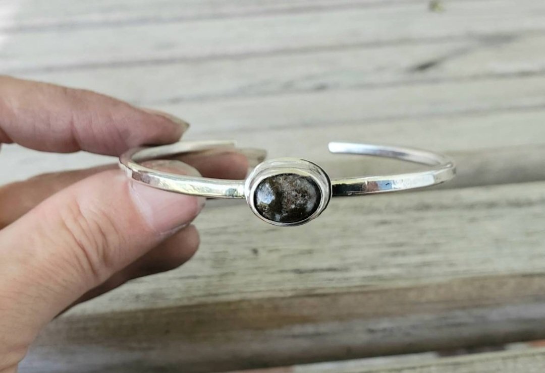 Black Agate Cabochon in Sterling Bezel Setting on a Sterling Silver Bangle Bracelet shown in model's hand over a wooden background