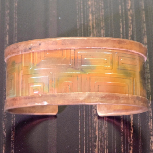 Folded and Textured Copper Bracelet that's been flamed painted for a multi colored look showing the rectangle textures up close.