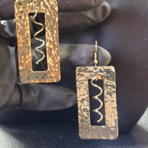 Hammered rectangle and spiral jeweler's brass on french wire earrings in model's hand to show lighting against the shiny hammered finish