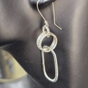 Textured Link Sterling Silver Earrings. French wire, attached to a loop, attached to two textured round rings, attached to one long textured oval shown on a mannequin to see the drop length.