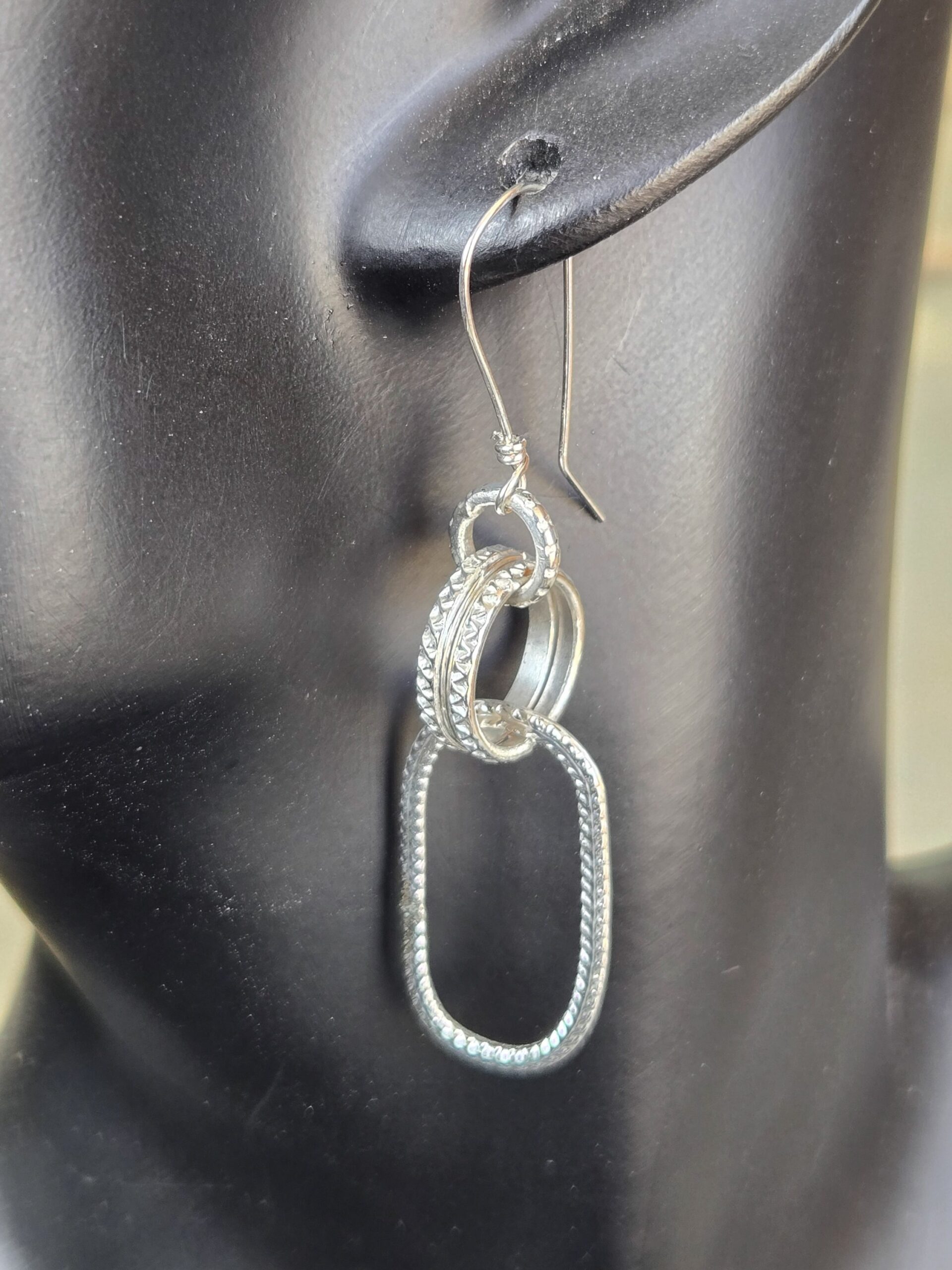 Textured Link Sterling Silver Earrings. French wire, attached to a loop, attached to two textured round rings, attached to one long textured oval shown on a mannequin to see how it drops.